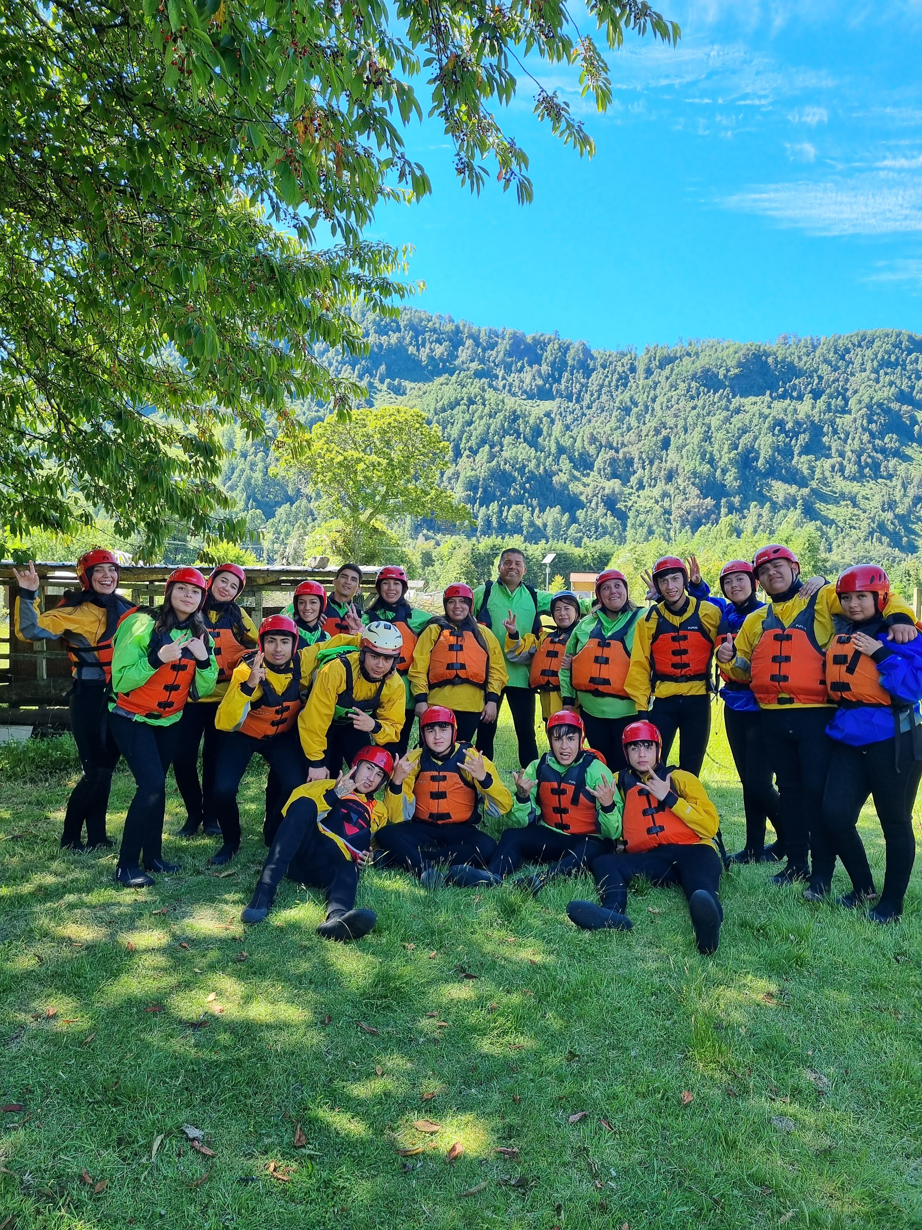 Grupo de estudiantes con cascos y chalecos de rafting posando en un prado