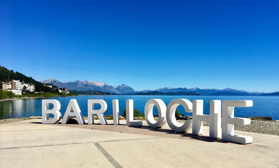 Letrero de Bariloche frente al lago Nahuel Huapi con la cordillera de los Andes al fondo